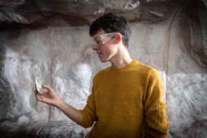 Male student examining a flint in front of the archaeology cave wall
